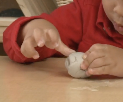 child pushing on small ball of clay